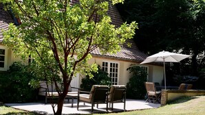 Un patio con mobiliario exterior, un árbol y una casa con tejado de baldosas.