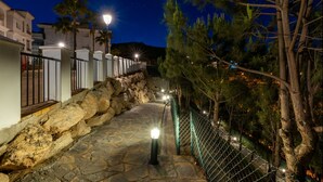 Un camí de pedra amb baranes metàl·liques i una tanca de filferro, que condueix a un edifici amb mur de pedra i una bandera.