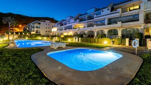 Zona piscina amb una piscina, gandules i un edifici amb balcons múltiples.