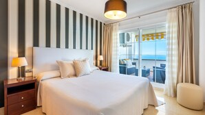 Una habitació d'hotel amb un llit gran, una tauleta de nit, una làmpada, una finestra amb cortines i un balcó amb vistes.