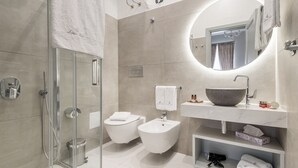 A modern bathroom with a glass-enclosed shower, a bidet, a sink with a large bowl, and a mirror with a round frame. - Lipari Suite  (Lipari)