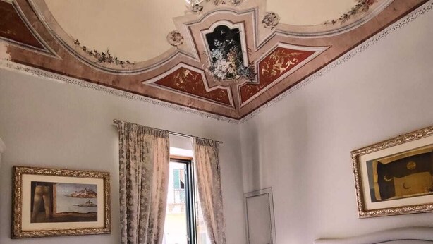 A hotel room with a large bed, a white chair, a nightstand, and a chandelier. - Lipari Suite  (Lipari)