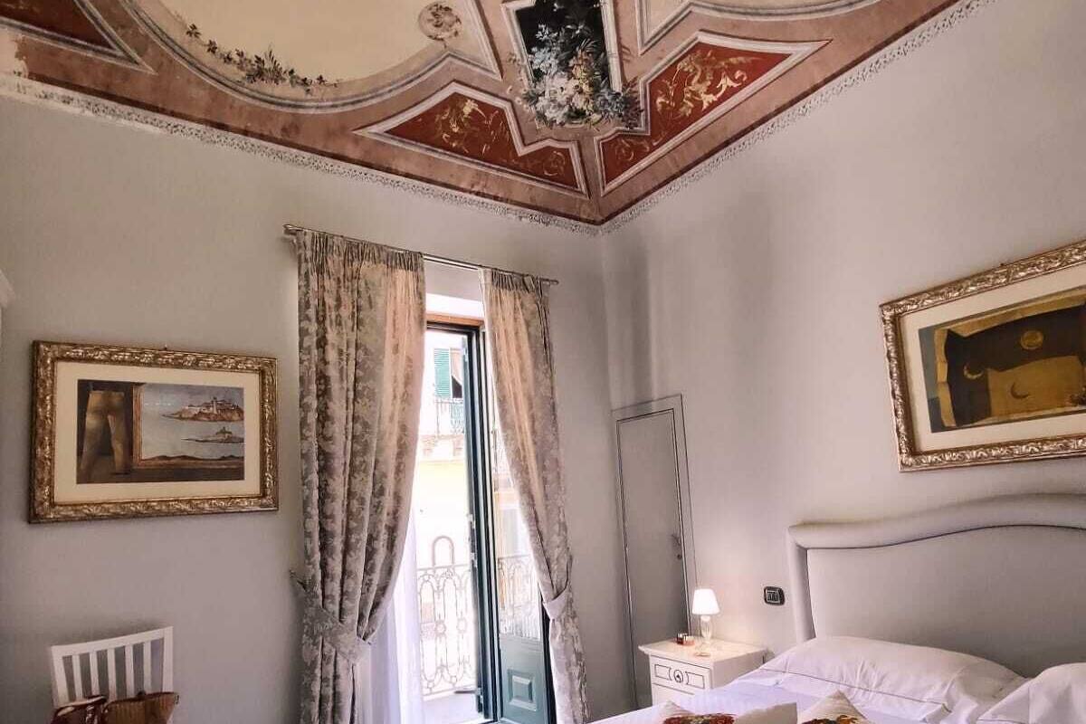 Una habitación de hotel con una cama grande, una silla blanca, una mesita de noche y un candelabro.
