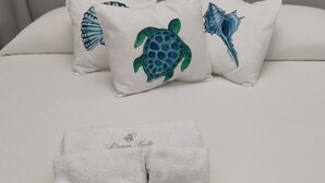 A bed with a grey headboard, two pillows with marine-themed designs, and two towels with text. - Lipari Suite  (Lipari)