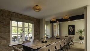 A long dining table with chairs, a brick wall, large windows, and a ceiling light fixture. - Het Landhuis by Interhome (Losser)