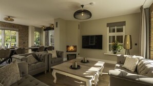 A living room with a fireplace, a television, and a dining area with a brick wall and large windows. - Het Landhuis by Interhome (Losser)