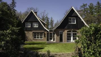 Stunning two-story house with a central entrance, flanked by large windows, set amidst a serene wooded area.