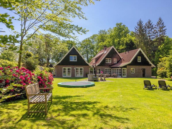A two-story house with a large lawn, a swimming pool, and a bench.