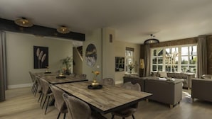 A spacious dining area with a long wooden table and modern chairs, a cozy living room with a sofa and a large window, and a staircase leading to an upper level. - Het Landhuis by Interhome (Losser)