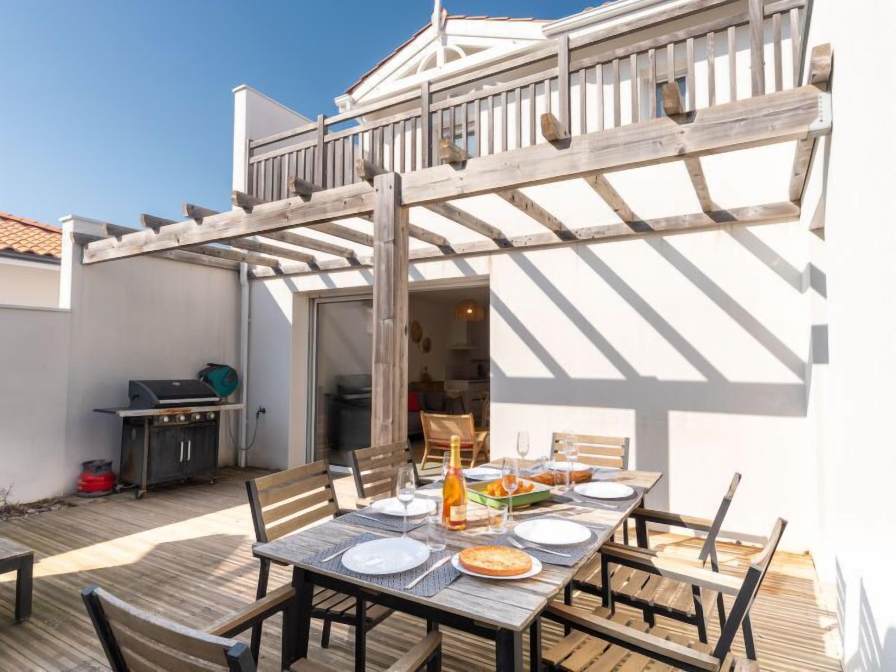 Zona de menjador a l'aire lliure coberta, amb taula de fusta per a dues persones, una barbacoa i un patio amb paviment de fusta.