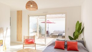 Un dormitorio moderno con una cama grande, una silla de madera, una mesa redonda de madera y un ventanal amplio.