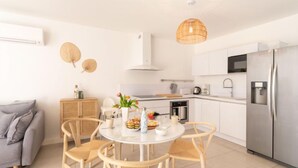 Una cocina moderna con armarios blancos, un refrigerador de acero inoxidable y una zona de comedor con una mesa redonda y sillas.