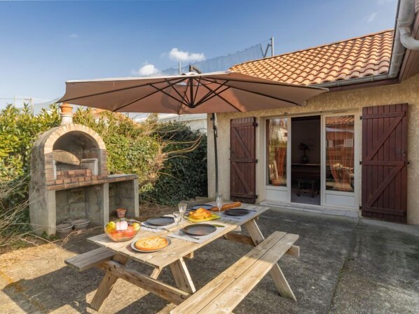An outdoor patio with a brick pizza oven, wooden table, and a large umbrella.