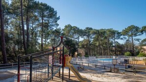 A playground with a slide and climbing net, surrounded by trees and a pool area. - Les Grands Pins by Interhome (Maubuisson)
