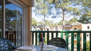 A table set for dining with plates, cutlery, and a wine bottle on a balcony with a view of buildings and trees. - Les Grands Pins by Interhome (Maubuisson)