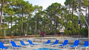 A swimming pool with blue and white lounge chairs, surrounded by a white fence and trees in the background. - Les Grands Pins by Interhome (Maubuisson)