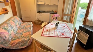 A compact living space with a sofa, a dining table with a placemat, a small kitchen area, and a radiator. - Moschettieri by Interhome (Bibione)