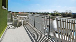 A balcony with a white table and chairs, a metal railing, and a view of buildings and trees. - Moschettieri by Interhome (Bibione)