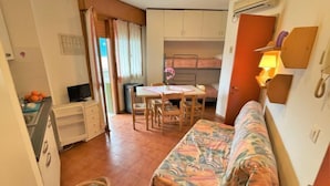 A compact room with a bed, a small table, a TV, and a kitchenette. - Moschettieri by Interhome (Bibione)