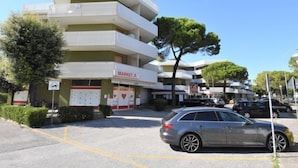 A multi-story building with a 'MARKET' sign, parked cars, and trees. - Moschettieri by Interhome (Bibione)