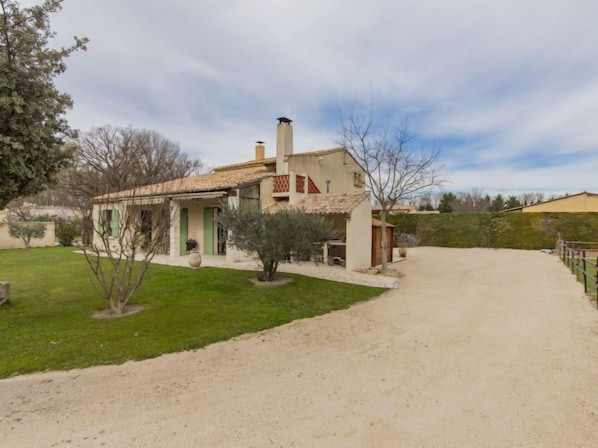 A two-story house with a tiled roof, a visible chimney, and a paved driveway leading to the entrance.