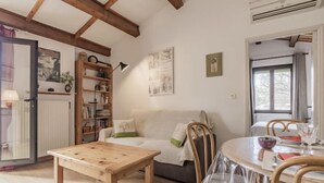 A cozy room with a wooden table, a sofa, and a dining table with chairs. There is a bookshelf and a radiator. - L'Aquillon by Interhome (Noves)