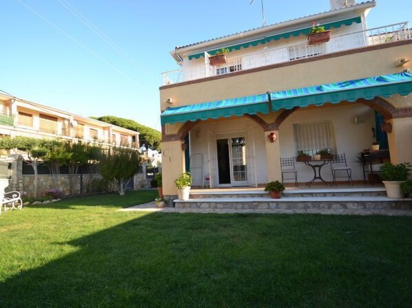 A two-story building with a covered patio area, a stone wall, and a well-maintained lawn.