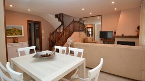 A dining area with a white table and chairs, a bowl of snacks, a staircase leading to another level, a sofa, and a television. - Vacation home Cuco by Interhome (Cambrils)
