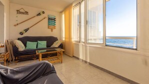 A room with a large window overlooking the sea, a sofa with cushions, a small table, and wall decorations including a sign with travel destinations. - Apartment Rits by Interhome (Salou)