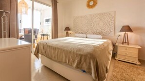 A bedroom with a bed, two bedside tables, a nightstand, a wall-mounted decorative piece, and a view of the outside. - Apartment Rits by Interhome (Salou)