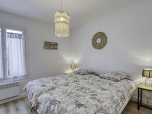 A bedroom with a bed, a hanging light fixture, a wall decoration, and a window with curtains.