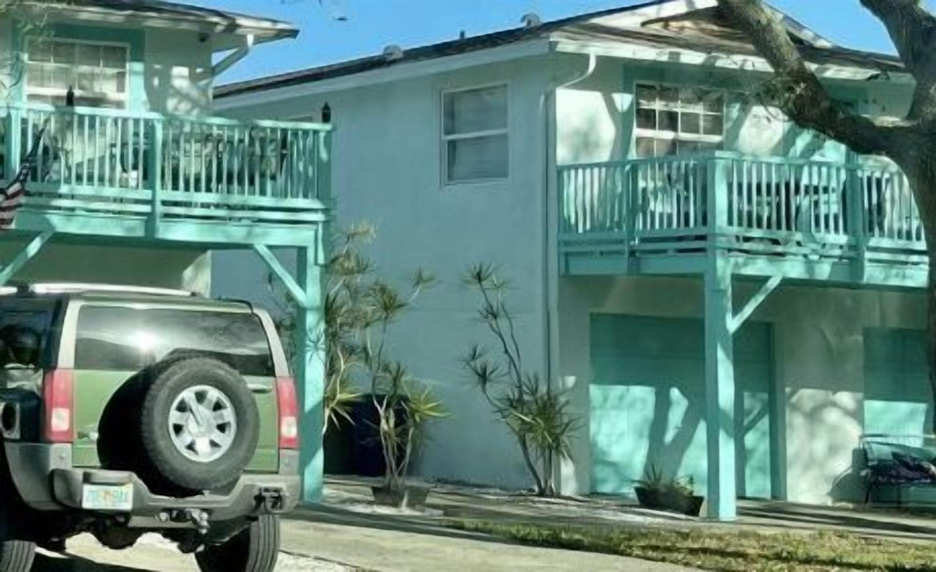 Una casa de dos pisos con un balcón y un SUV estacionado.