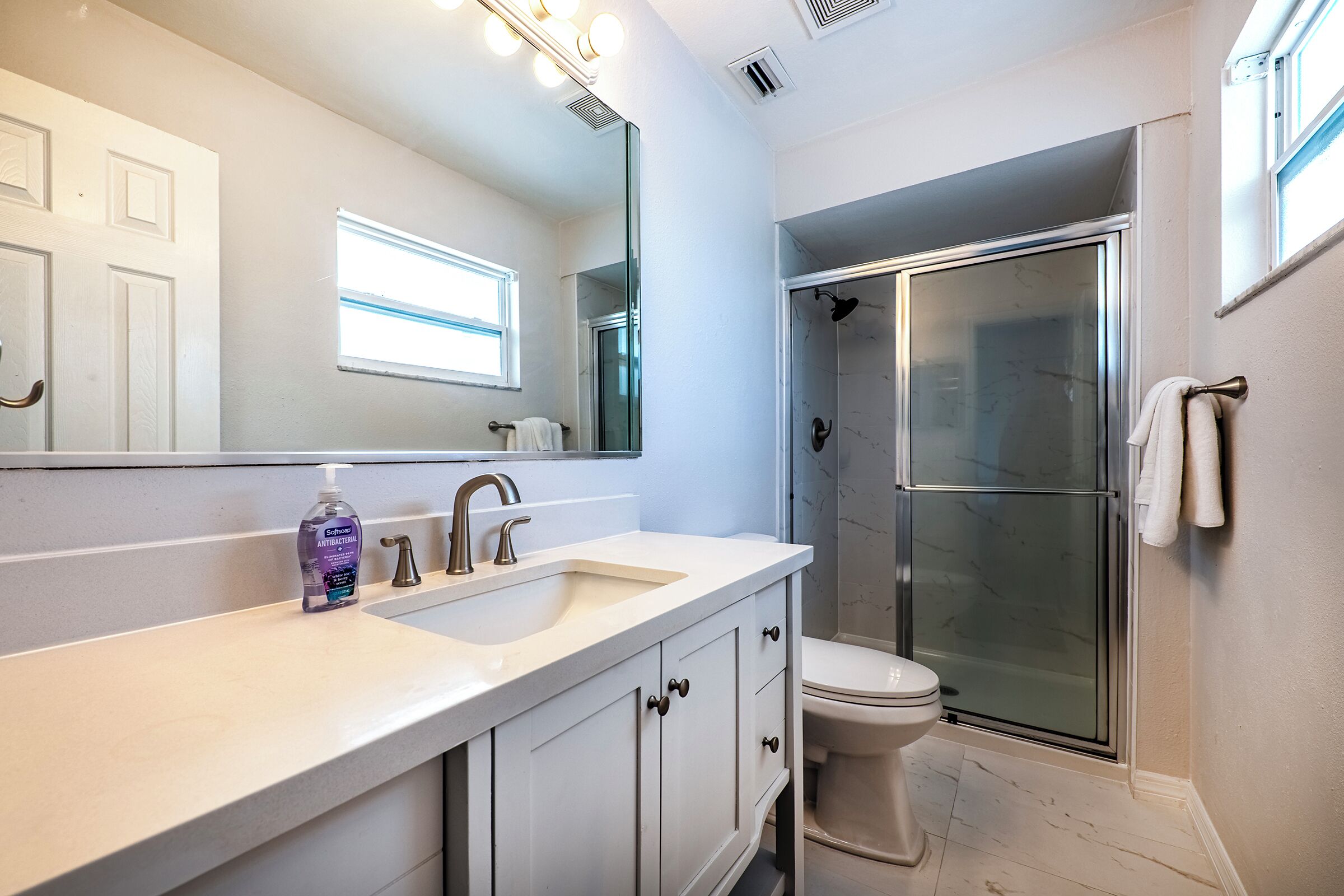 Een moderne badkamer met een wit wastafelmeubel, een grote spiegel, een douchecabine van glas en een toilet.