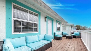 A covered outdoor deck with a light blue sofa and matching cushions, a wicker chair, and a small table. - Spacious 2-bed, 2-bath second-floor unit minutes from Indian Rocks Beach. Sleeps nine with full kitchen, WiFi, smart TVs, parking, beach gear, and direct pool access. A bright, comfortable base for families and groups (Indian Rocks Beach)