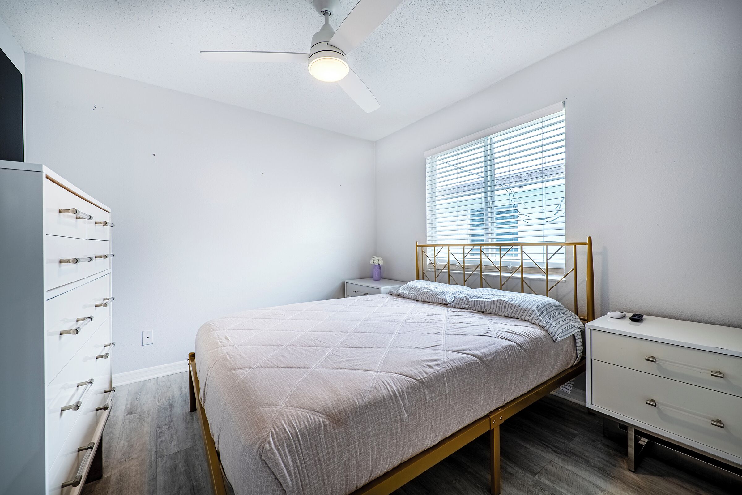 Ein Schlafzimmer mit Bett, Nachttisch, Kommode und Deckenventilator.