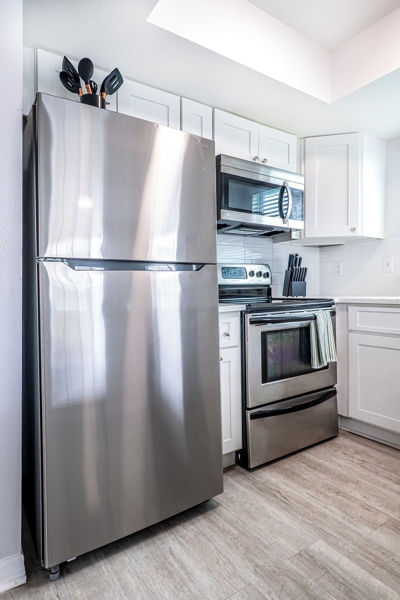 A modern kitchen with stainless steel appliances, white cabinets, and a wooden floor.