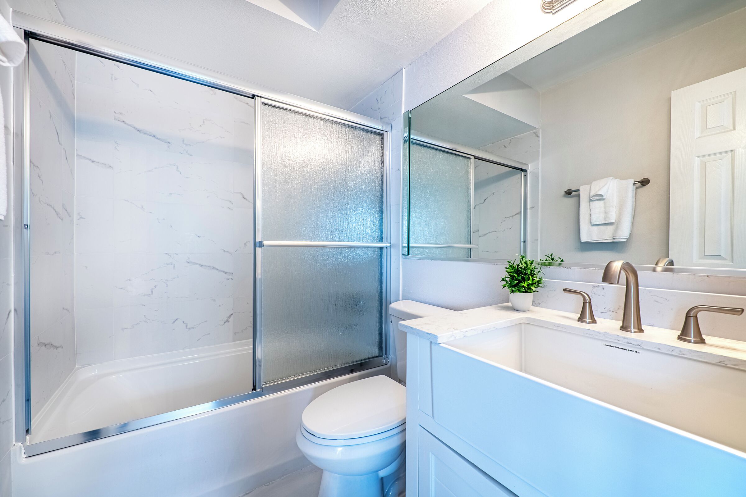 A modern bathroom with a glass-enclosed shower, a white toilet, and a sink with a mirror above it.