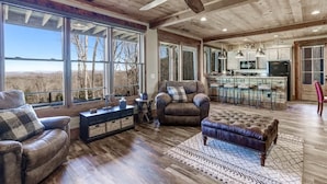 A spacious living room with leather furniture, large windows, and a ceiling fan.