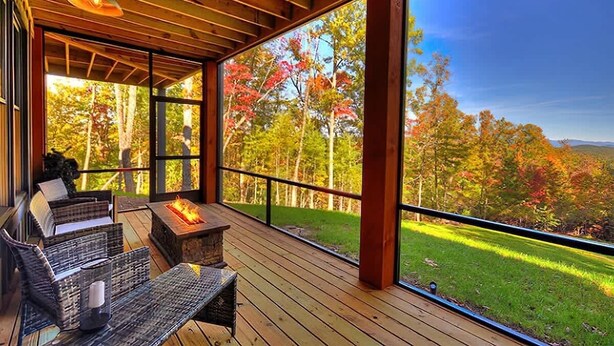 Une terrasse en bois avec des sièges extérieurs et un foyer, offrant une vue sur un paysage boisé.