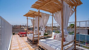 A rooftop terrace with a wooden canopy bed, a small seating area, and a view of the cityscape. - Riad Villa Saphir (Marrakech)
