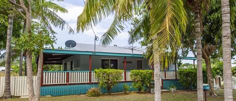 A house with a porch, surrounded by palm trees and a fenced yard.