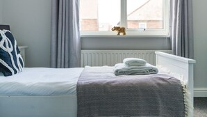 A neatly made bed with a patterned bedspread, a folded white towel, and a small figurine on the windowsill. - Lily Apartment 2 - 2 bed flat Bedlington (Bedlington)