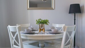 A dining table with white chairs, a vase with green plants, and a framed mirror above it. - Lily Apartment 2 - 2 bed flat Bedlington (Bedlington)