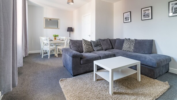 A modern living room with a grey sofa, a white coffee table, and a dining area with a white table and chairs. - Lily Apartment 2 - 2 bed flat Bedlington (Bedlington)