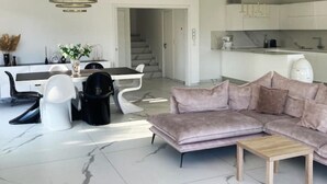 Een moderne woonkamer met een bank, een salontafel, en een eethoek met een tafel en stoelen.