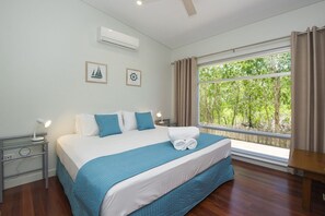 Ein Schlafzimmer mit einem großen Bett, einem Nachttisch mit Lampe, einer Klimaanlage und einem Fenster mit Vorhängen.