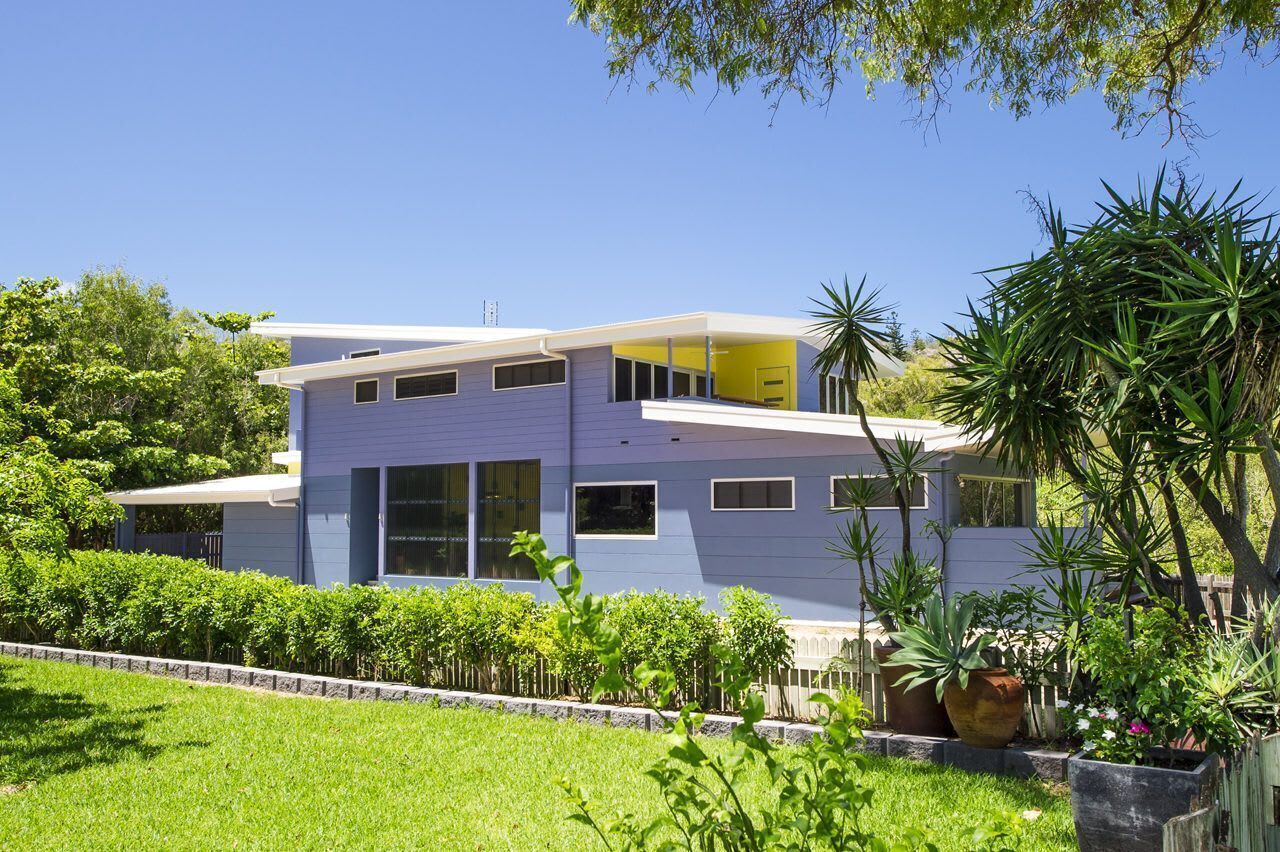 Une maison moderne à deux étages, dotée d’un toit plat, de grandes fenêtres et d’un balcon.