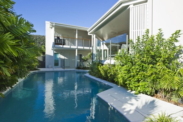 Una casa moderna de dos pisos con piscina, rodeada de abundante vegetación.