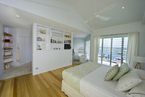 Un dormitorio con cama, ventilador de techo, ventana con vista a barcos y estanterías empotradas.