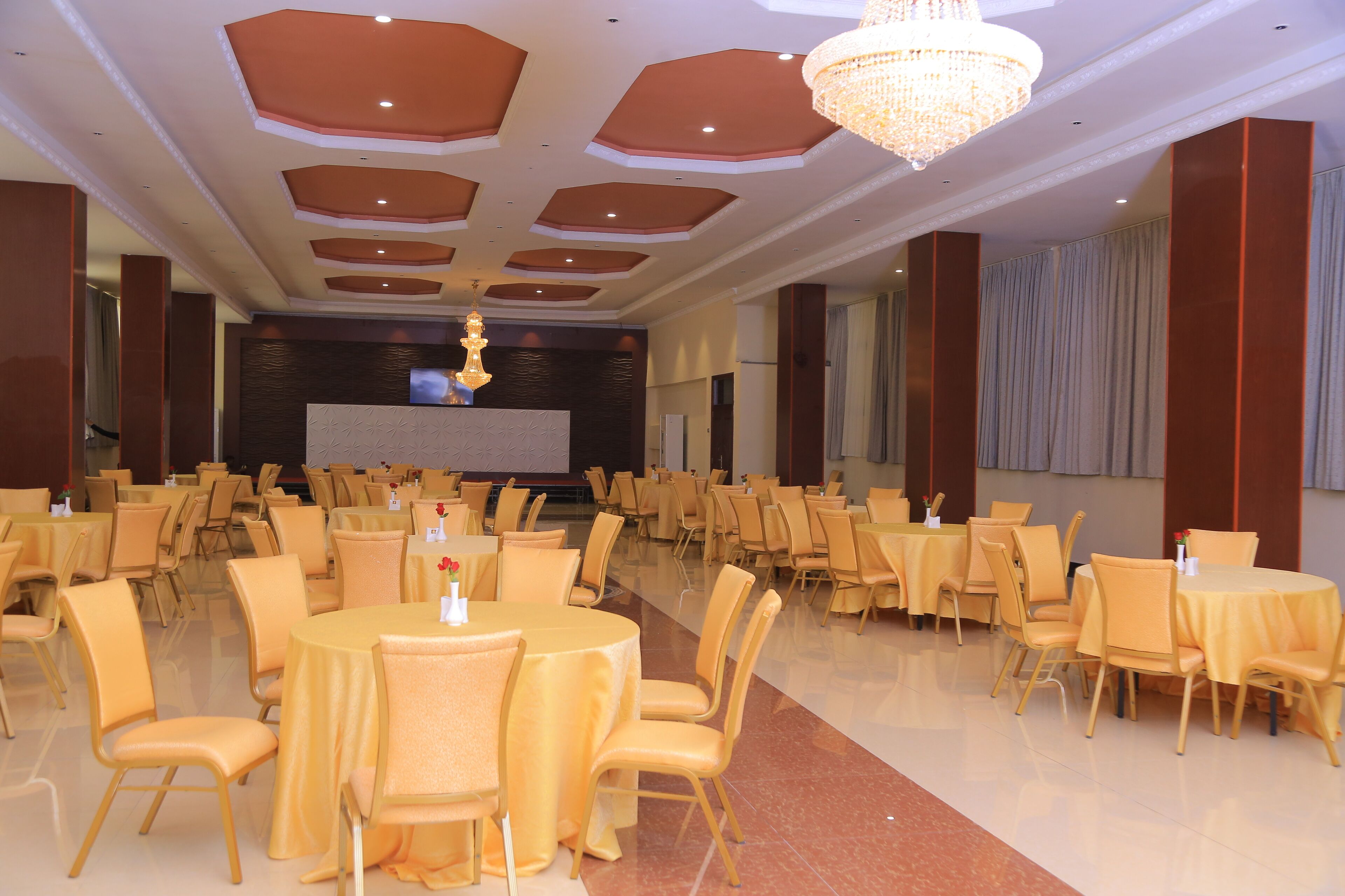 Une salle de banquet avec des tables et des chaises rondes, une scène et un lustre.